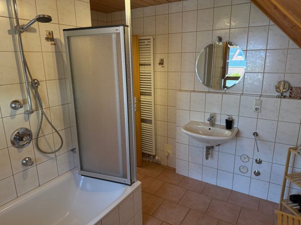 Badezimmer Badezimmer mit Dusche, Badewanne, Waschbecken und runder Spiegel, gefliest.