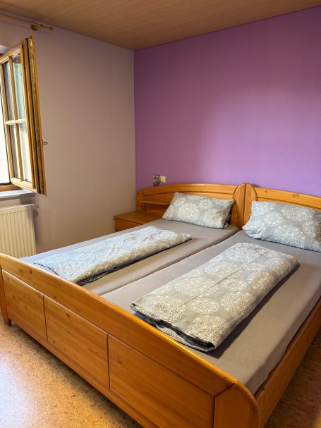 Großes Schlafzimmer Doppelbett mit grauen Bettwäsche in einem Raum mit lila Wänden.