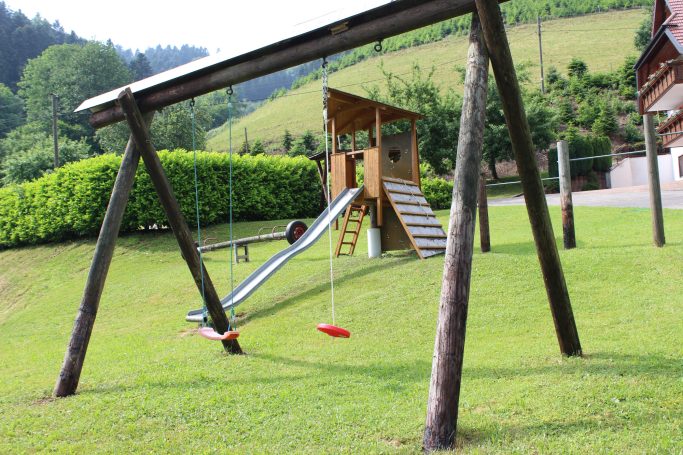 Spielplatz Ein Spielplatz mit einer Rutsche, Schaukeln und grüner Umgebung.