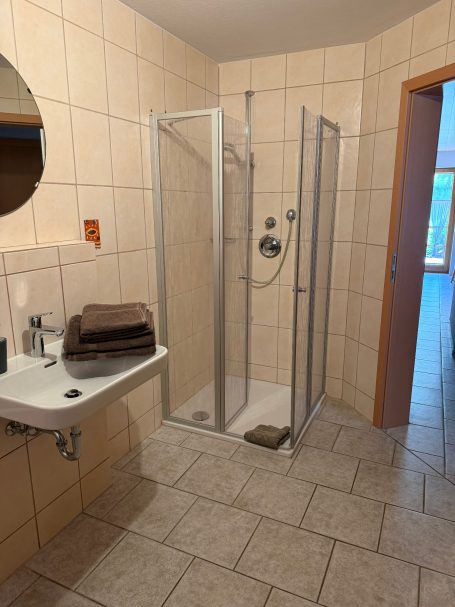 Badezimmer Badezimmer mit Dusche, Waschbecken und gefalteten Handtüchern auf dem Boden.