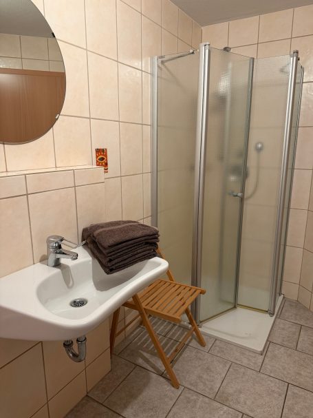 Badezimmer Badezimmer mit Dusche, Waschbecken und einem Holzstuhl mit Handtüchern.