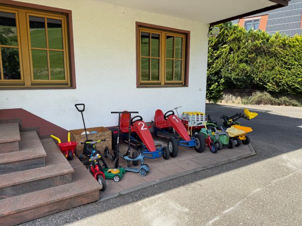 Der Kinder-Fuhrpark Rote Roller und Spielzeugfahrzeuge stehen an einer Wand neben einer Treppe.