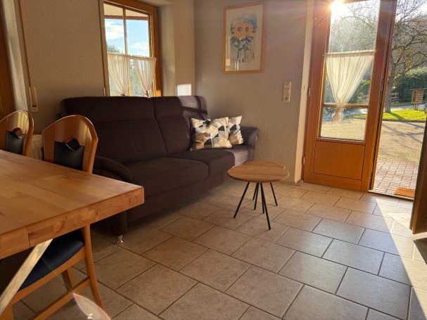 Großes Wohn-/ Esszimmer Gemütliches Wohnzimmer mit dunklem Sofa, Tisch und Fenster zur Terrasse.