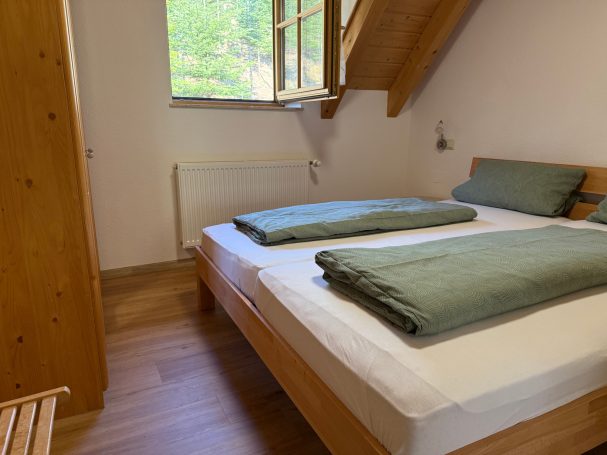 Schlafzimmer 2 Helles Schlafzimmer mit zwei Betten und grünen Bettdecken, Holzdetails und Fenster.