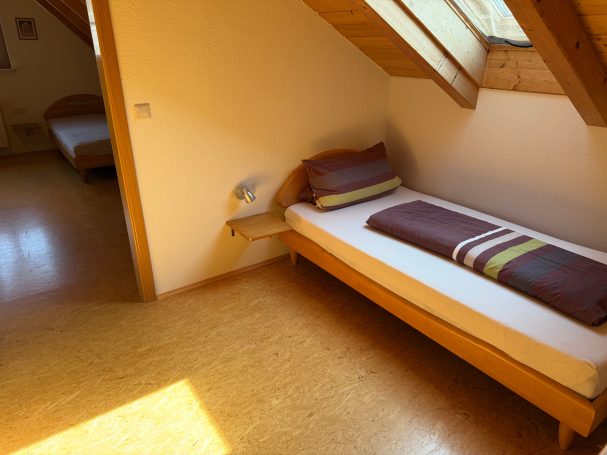 Durchgangszimmer mit 2 Einzelbetten Ein einfaches Schlafzimmer mit einem Einzelbett und einem zweiten Bett im Hintergrund.