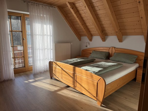 Ferienwohnung 2 Helles Schlafzimmer mit Holzbalkendecke, Doppelbett und Balkon.