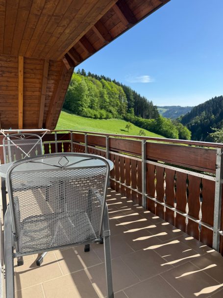 Großer Balkon Balkon mit Metallmöbeln und Blick auf grüne Hügel unter klarem Himmel.