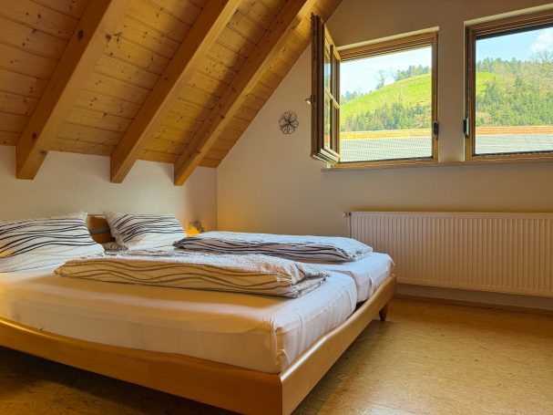 Schlafzimmer mit Doppelbett und Einzelbett Helles Schlafzimmer mit Holzdecke, zwei Einzelbetten und Fenster mit Ausblick ins Grüne.