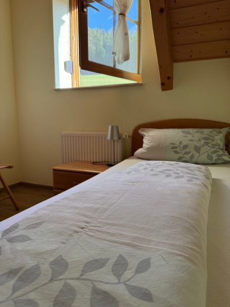 Kinderzimmer Ein schlichtes Schlafzimmer mit einem Einzelbett, einem Fenster und natürlichem Licht.