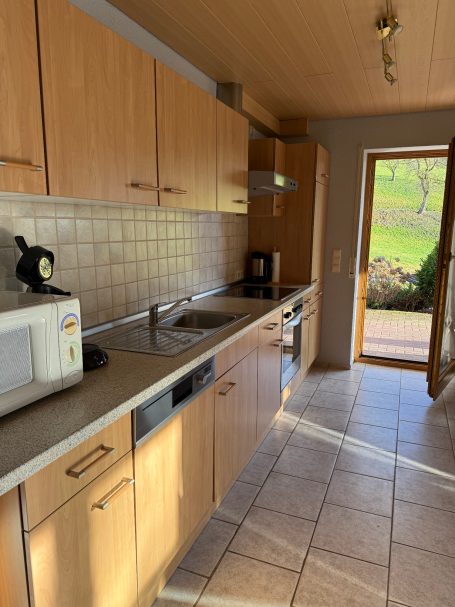 Große Küche Helle Küche mit Holzschränken, Mikrowelle, Spüle und Zugang zur Terrasse.